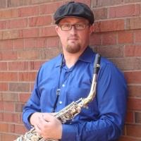 Teacher Kevin Norton holding his sax while leaning against a brick wall