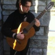 Teacher Bryan Henry playing his guitar in front of a stone wall