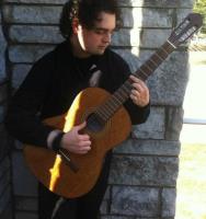 Teacher Bryan Henry playing his guitar in front of a stone wall